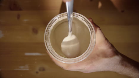 vertical, de arriba hacia abajo: concéntrese en el borde del frasco, se mezcla el iniciador de masa fermentada, se levanta la cuchara