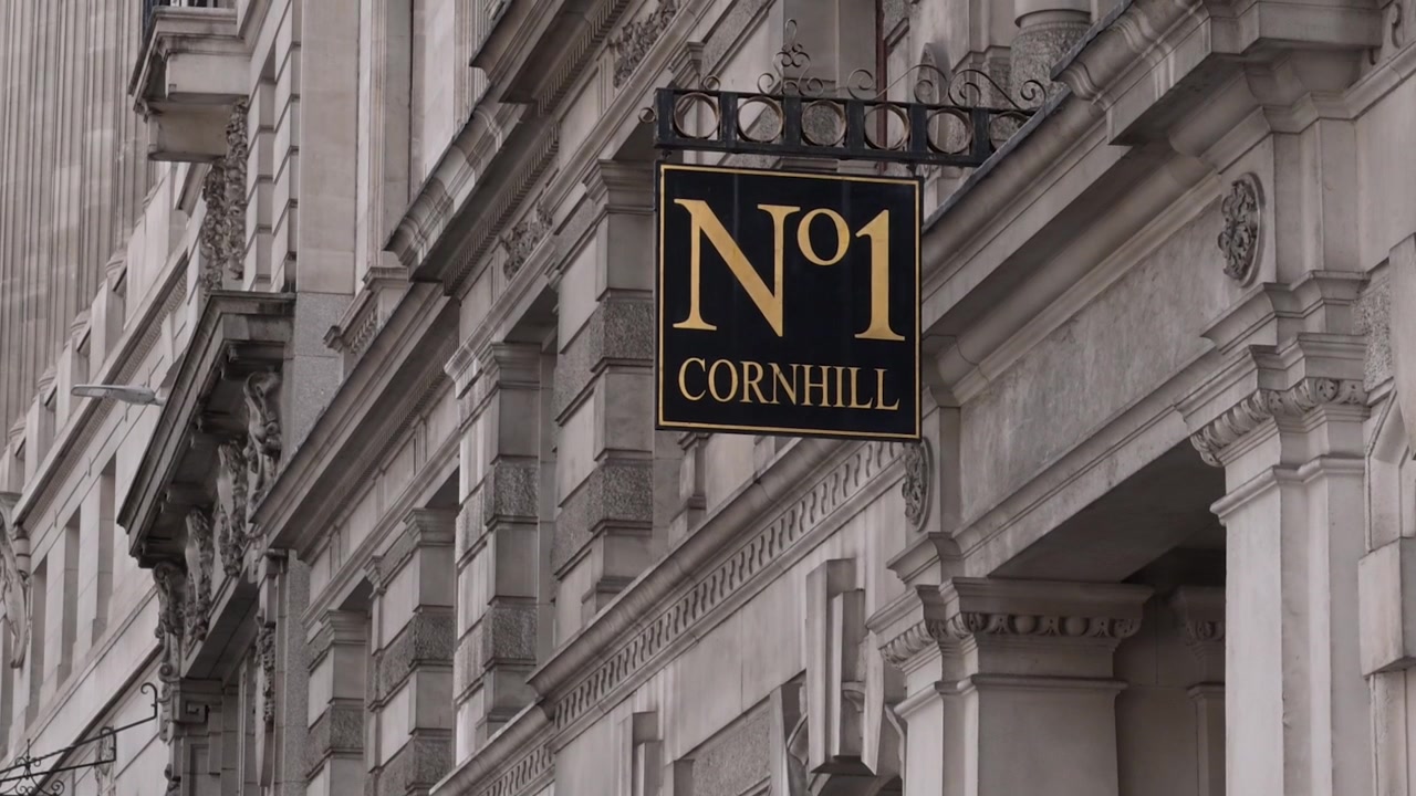 Insegna nera e oro "1 Cornhill" appesa a una staffa ornata su un edificio in pietra dettagliato nel distretto finanziario della City di Londra.