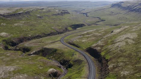 Looking-over-a-curvey-twisting-road-cutting-through-an-empty-valley-in-Iceland-on-a-cloudy-summer-evening