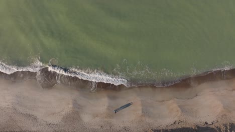 aerial view two people slowly walk across the sand, and sea waves are washing the shore of the beach on a cold autumn morning