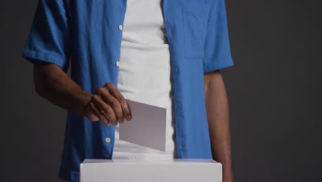 Close-Up-Of-Man-Casting-Vote-Into-Election-Ballot-Box-Against-Black-Background-In-Slow-Motion