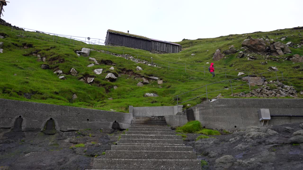 Woman descends stairs to the natural pier of Mykines to board a ferry to Sorvagur in Vagar Island