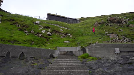 Una-Mujer-Baja-Las-Escaleras-Hasta-El-Muelle-Natural-De-Mykines-Para-Abordar-Un-Ferry-A-Sorvagur-En-La-Isla-De-Vagar.