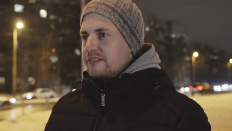 casual caucasian man in 30s outdoors in a street on cold evening talks and sighs