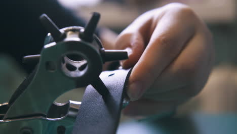 Skilled designer makes holes in stylish leather belt closeup