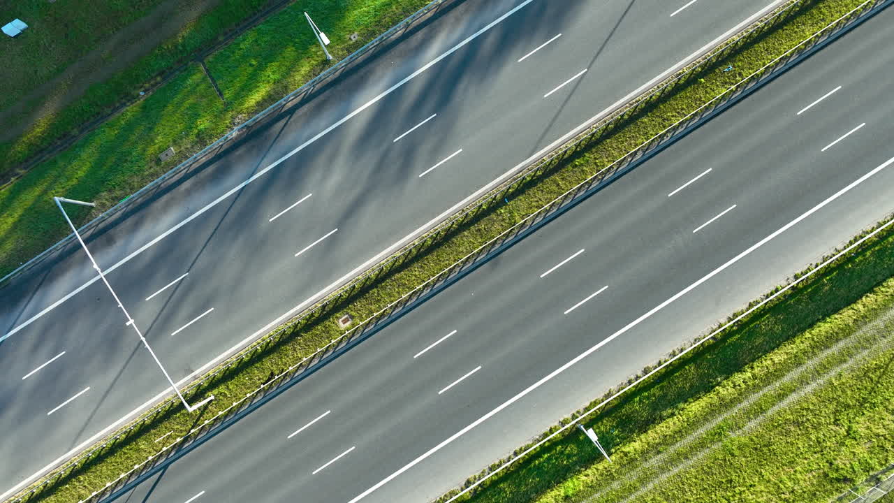 Drone shot of multiple cars traveling on wide multi‑lane highway divided by grassy median under clear daylight