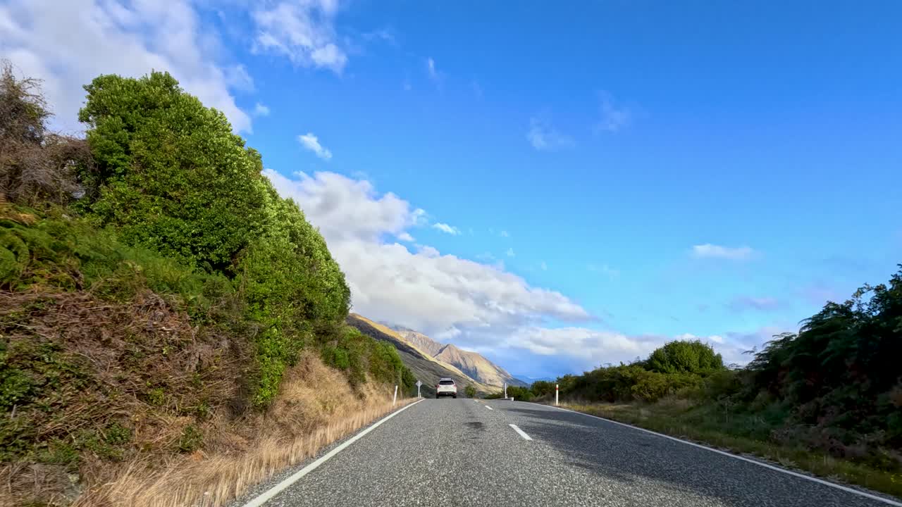 Vehicle travels winding mountain road with lake views, lush greenery, and bright daylight, steady perspective