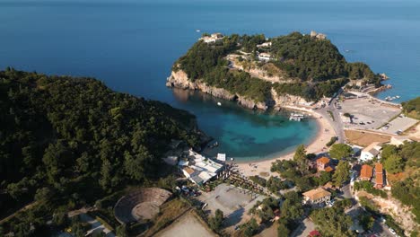 Una-Rápida-Panorámica-Aérea-Establece-Una-Cala-De-Arena-Protegida-Y-Una-Playa-Con-Barcos-En-El-Muelle-Y-Gente-Relajándose-En-Corfú,-Grecia.