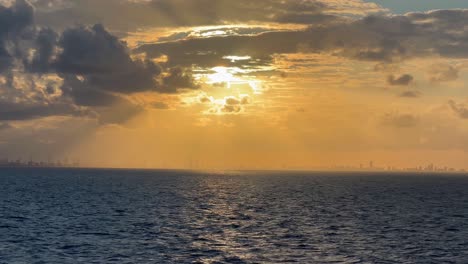 la ciudad de miami florida paisaje urbano vista desde el océano contorno lejano horizonte épico cinematográfico agua naranja amanecer puesta de sol nubes rayos de luz gloriosos