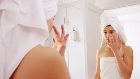 mujer aplicando crema hidratante en su cara en el baño