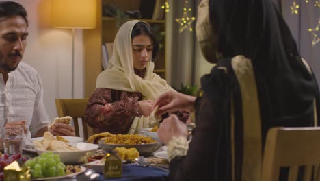 familia musulmana sentada alrededor de una mesa en casa comiendo comida para celebrar eid