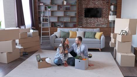 una pareja joven desempaquetando una caja de cartón y discutiendo el diseño de interiores en un nuevo apartamento el día de la mudanza. propietarios felices el día del traslado. concepto de bienes raíces y alquiler. préstamo hipotecario para familia joven.