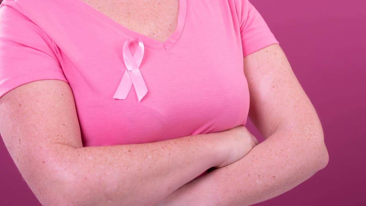 Video del mezzo busto di una donna caucasica con le braccia incrociate che indossa un nastro rosa per la sensibilizzazione al cancro.