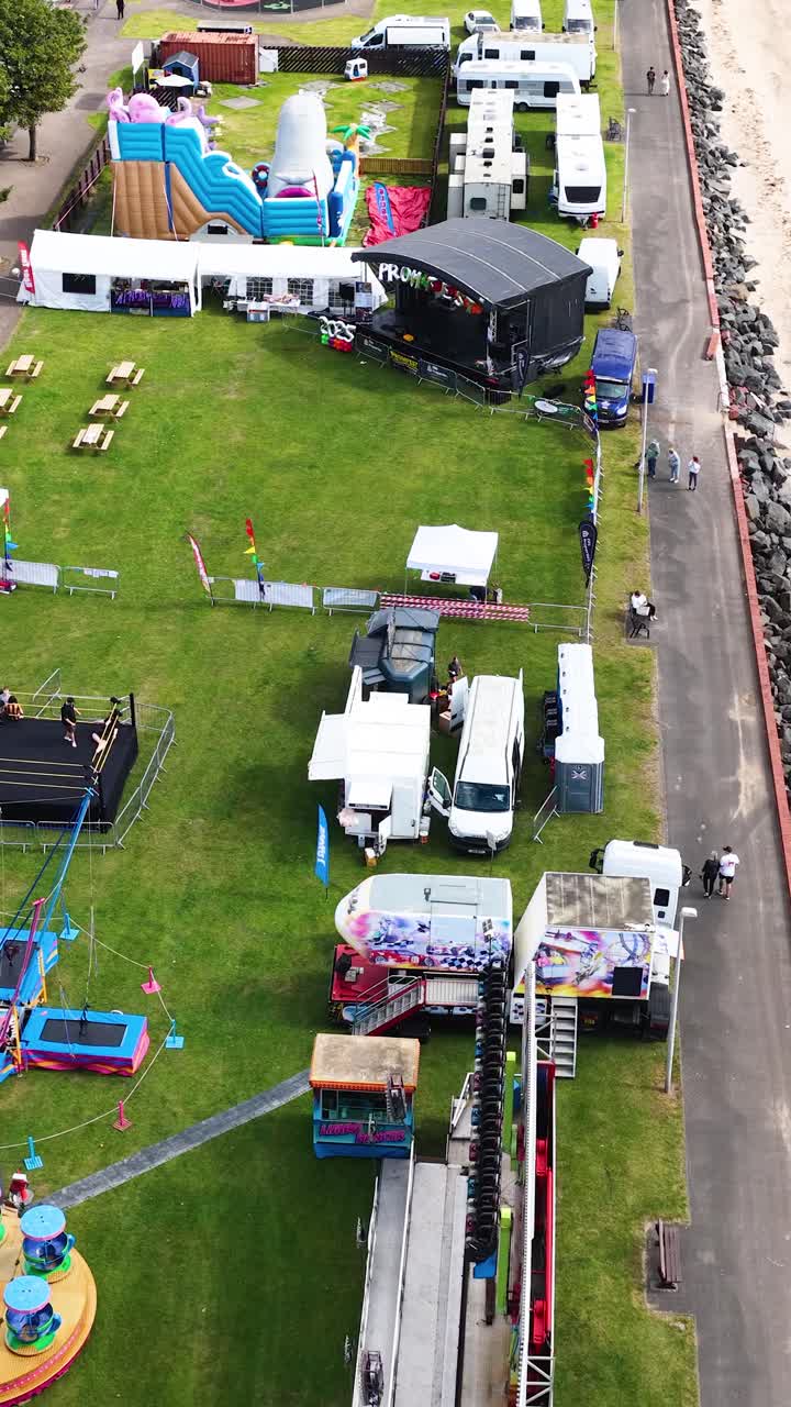 Drone captures vibrant fairground, tents, and beach with gentle camera movement, bright daylight, wide perspective