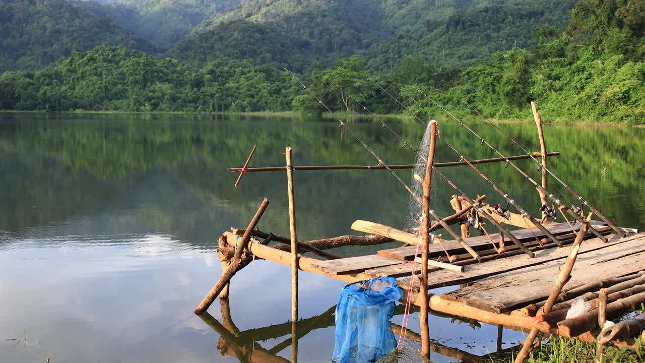 un grupo de cañas de pescar en el muelle esperando pescar en un lago con fondo forestal