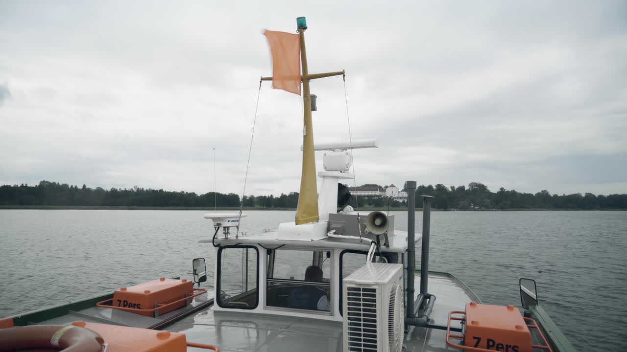 Smooth shot of transport ship cruising on the lakeChiemsee in Germany towards the famous Herreninselduring a cloudy day in the morning
