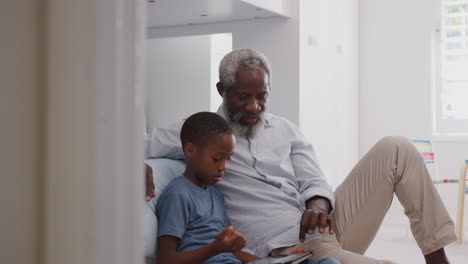 Abuelo-Sentado-Con-Su-Nieto-En-El-Dormitorio-De-Los-Niños-Usando-Una-Tableta-Digital-Juntos