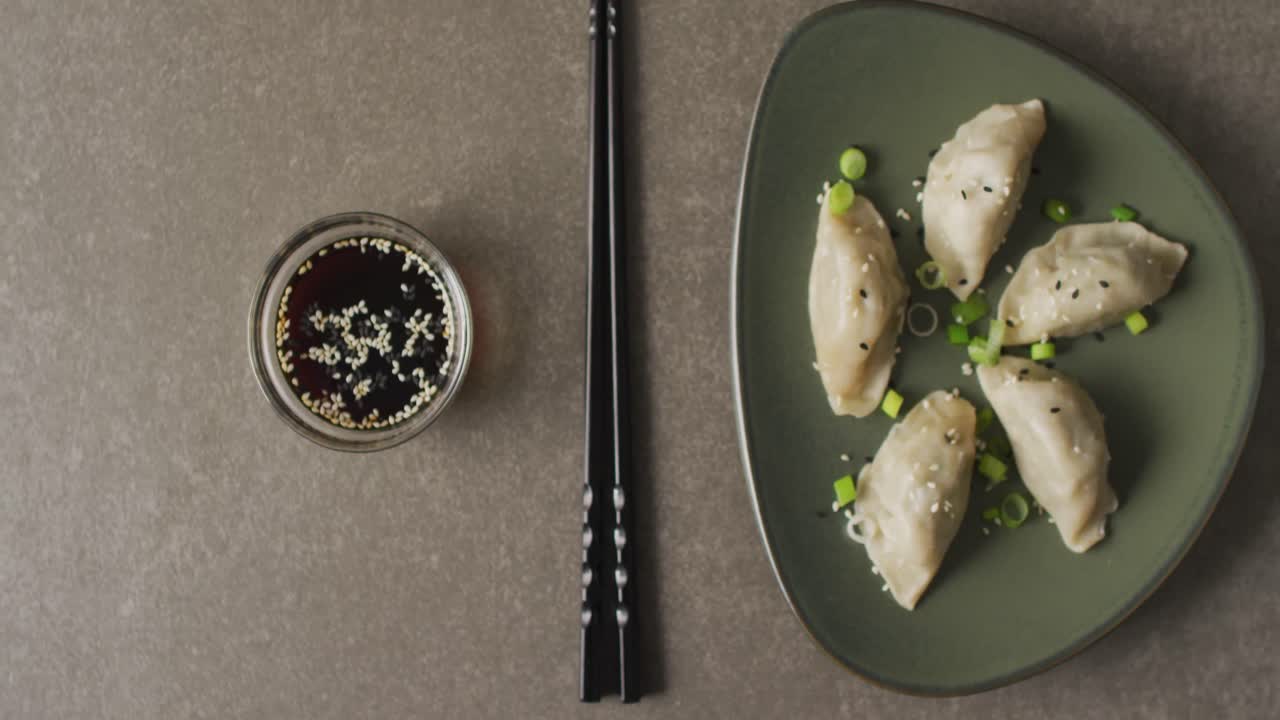 Composition of plate with gyoza dumplings and soy sauce with chopsticks on grey background