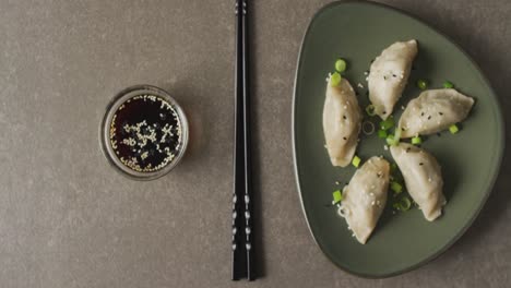 Composition-of-plate-with-gyoza-dumplings-and-soy-sauce-with-chopsticks-on-grey-background