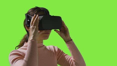 mujer poniendo auriculares de realidad virtual y mirando a su alrededor contra el fondo del estudio de pantalla verde 2
