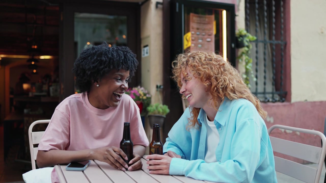 Two Happy Young Women Laughing and Talking at an Outdoor Cafe