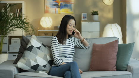 Junge-Frau-In-Gestreifter-Bluse-Sitzt-Auf-Sofa-Im-Wohnzimmer-Und-Telefoniert-1