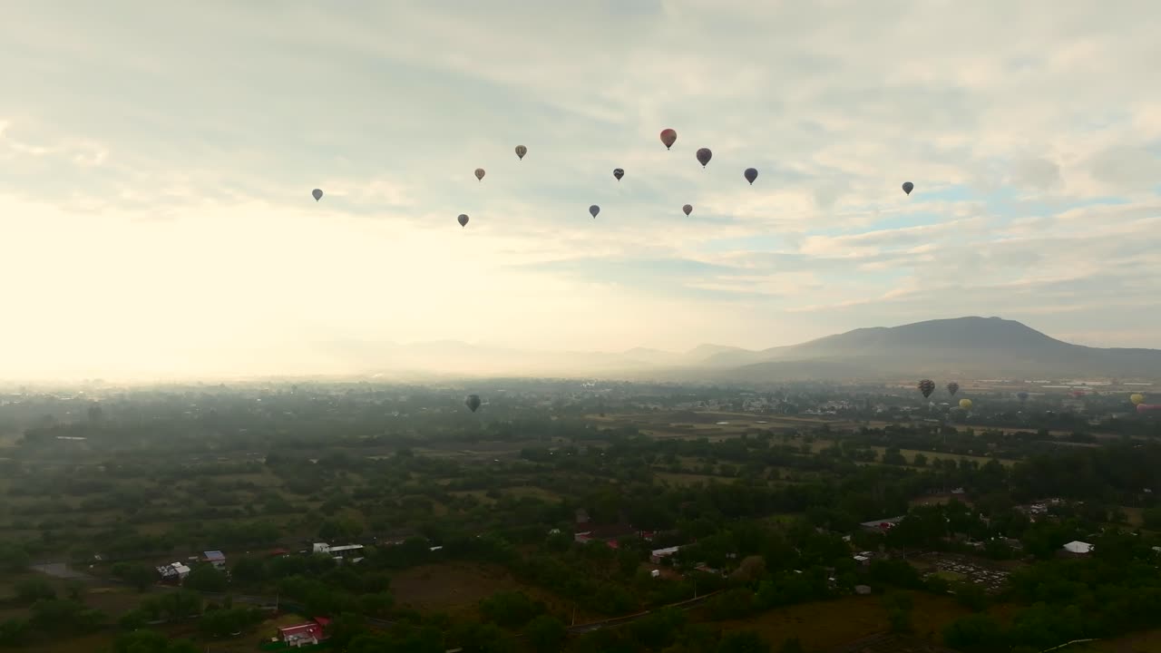 Hot air balloons flying atop lush green park around Teotihuacan, Mexico. Dolly in, ascending drone aerial