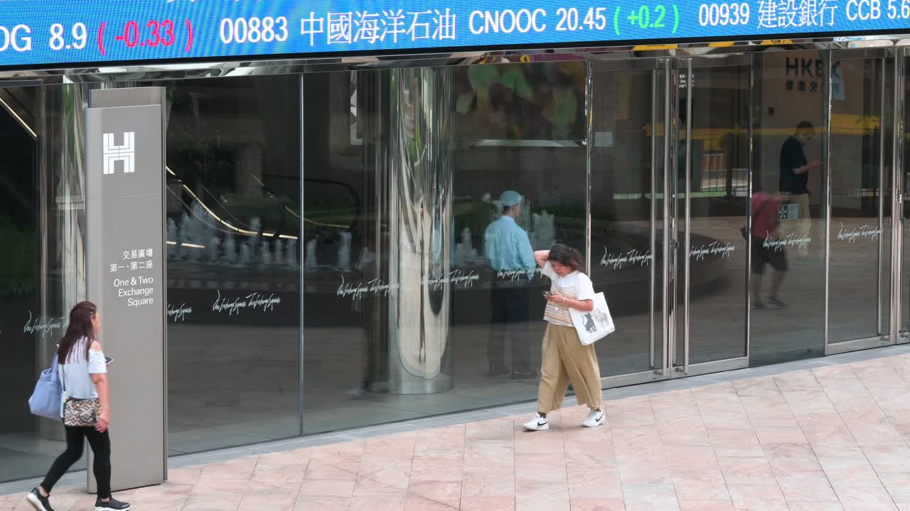 A moving screen displaying negative stock ticker symbols captures the attention of passersby at Exchange Square, home to the Hong Kong Stock Exchange (HKEX) in the financial district of Hong Kong.