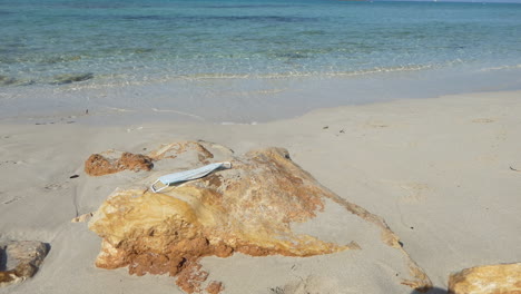 surgical mask polluting a beautiful beach with blond golden sand and crystal clear water