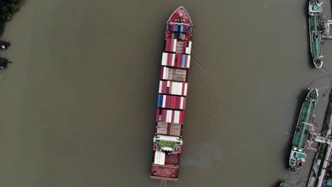 top view pointing down over container carrier ship cruising along chao phraya river heading to port of bangkok, thailand