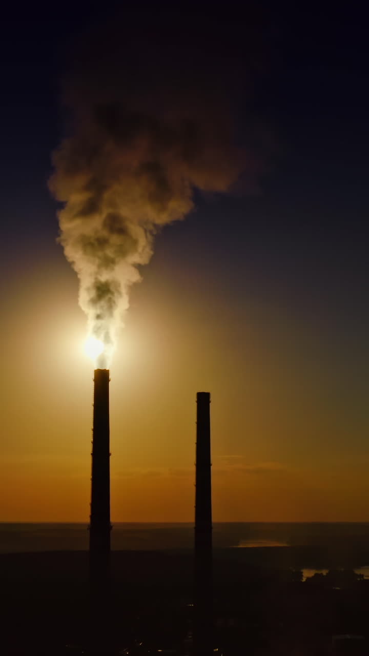 Massive smoke from stacks against the moon. Dark silhouette of industrial tower pipes at night. Thick fumes going into the air in the evening. Ecological disaster. Aerial view. Vertical video