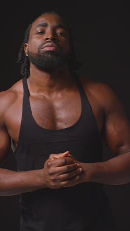 vertical video portrait of male athlete wearing fitness vest with muscular physique walking towards camera and into focus training for sports event against black studio background