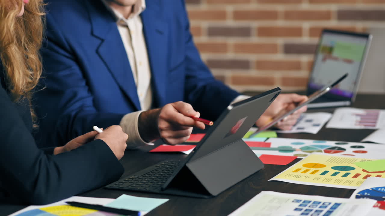 Forretningsmøde på et kontor. Kvinde og en mand gestikulerer og diskuterer forretningsanliggender. Tablet og papirer med grafer og noter.