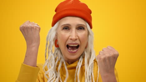 Joyful-old-woman-shouting-in-modern-studio.-Happy-lady-raising-fists-indoors.