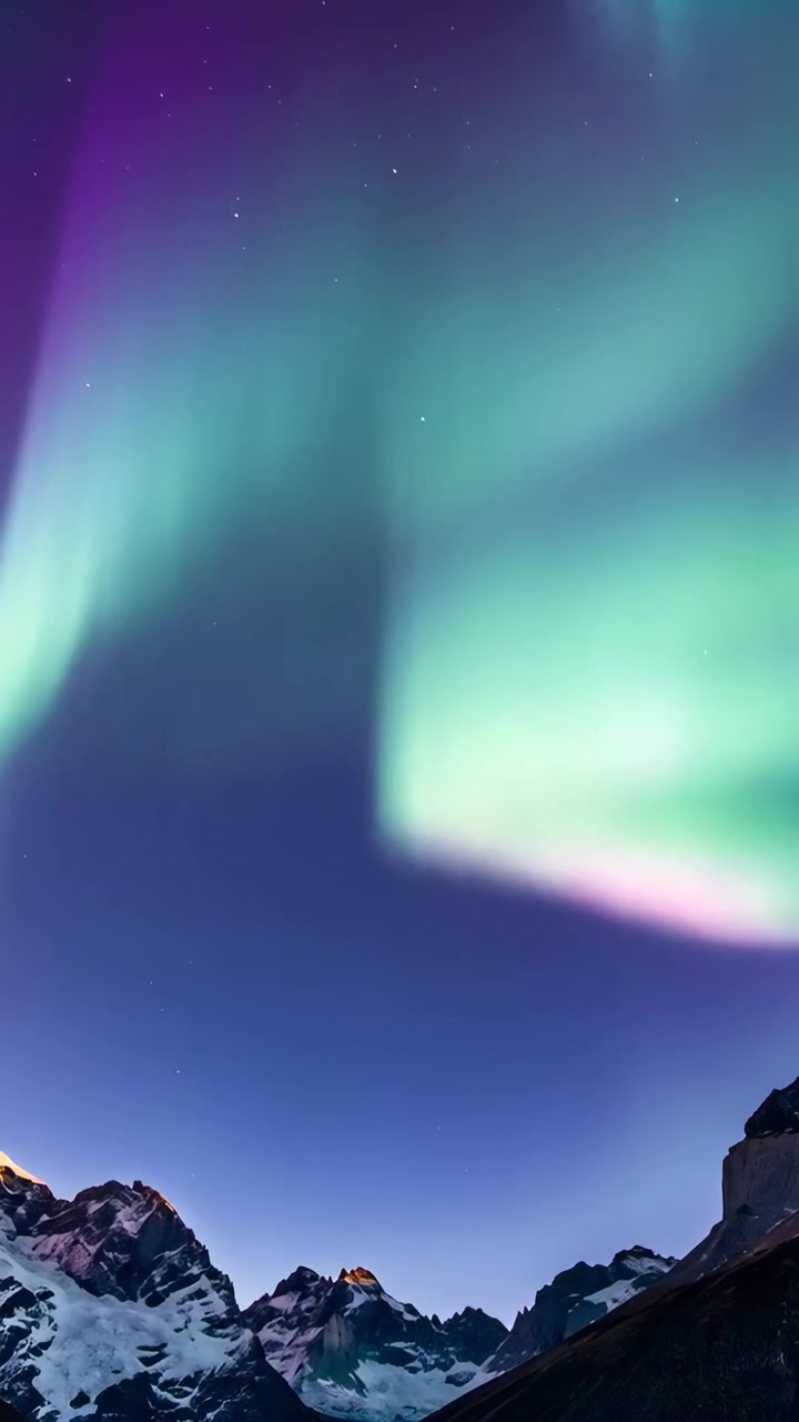 Video verticale: Aurora ascendente che scorre dalle cime innevate, espandendosi in un nastro verde-viola.