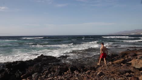 Eine-Person-An-Einem-Felsigen-Strand-Mit-Starken-Wellen-Wird-Fühlen,-Ob-Das-Wasser-Warm-Ist