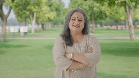 happy indian old woman standing crossed hands in park