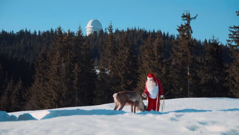 santa claus and one of his deer are standing on a snowy slope