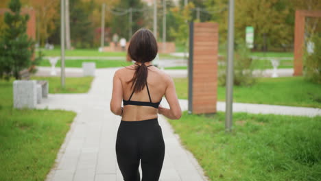 back view of athletic woman running in park with decorative benches and poles in background, ideal for fitness, outdoor workouts, and active lifestyle content in green urban park setting