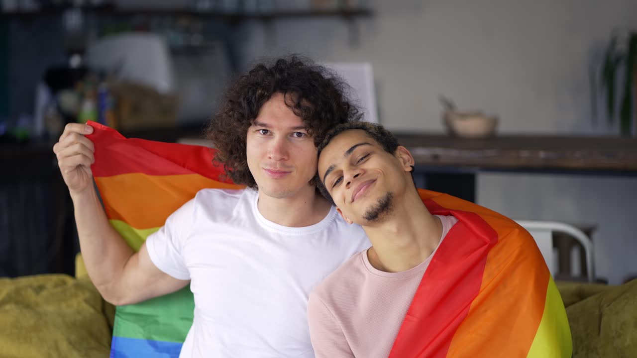 Guys spend time together at home on the couch under lgbt colorful rainbow flag