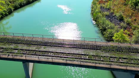 Vista-Aérea-De-La-Vía-Férrea-Abandonada-Cubierta-De-Hierba-En-El-Puente-Sobre-Un-Río-Tranquilo-Y-Limpio