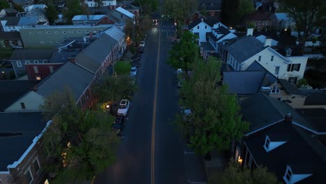 Aerial-night-view-of-a-small-American-town-with-a-dark-street-lined-with-trees-and-buildings