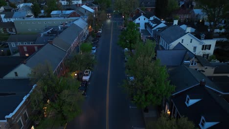 aerial night view of a small american town with a dark street lined with trees and buildings