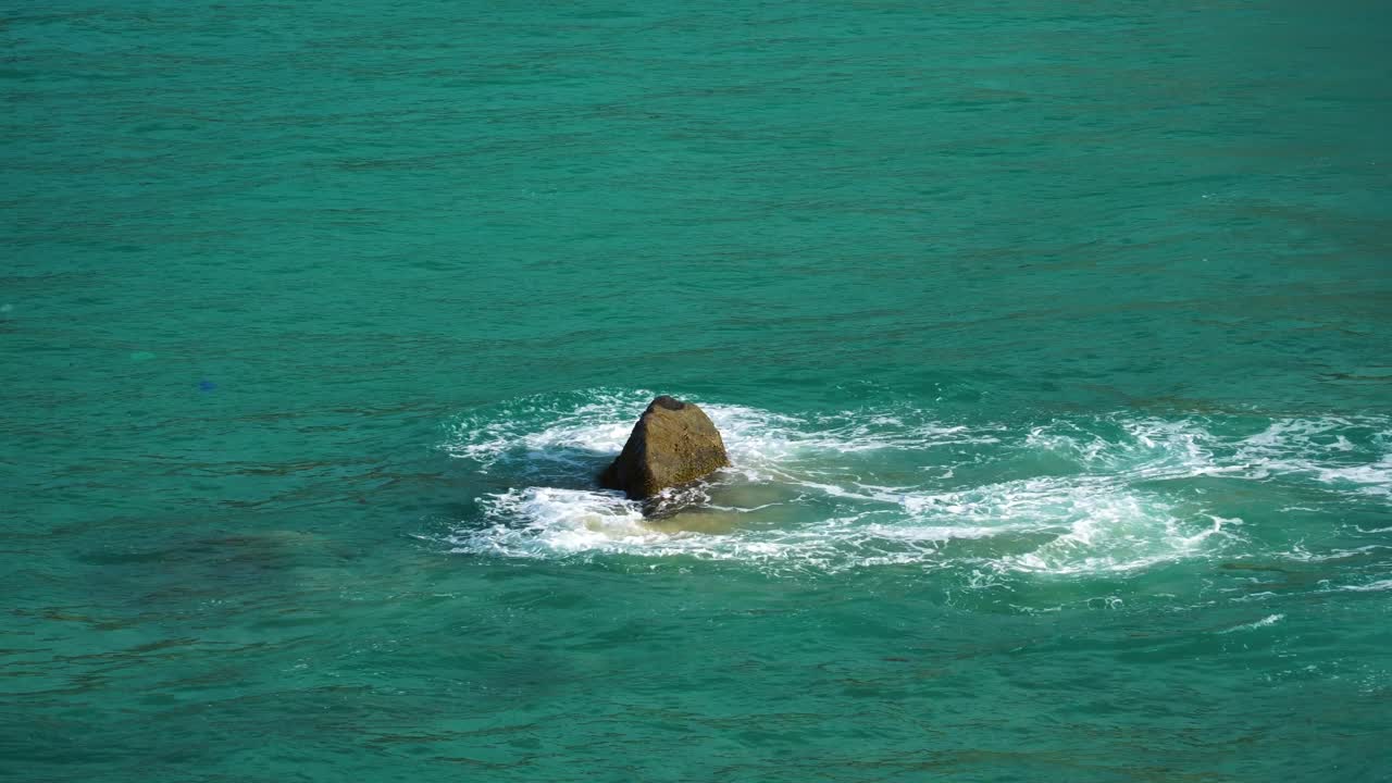 날카로운 바위를 통해 부드러운 바다 물결이 튀고, 에메랄드 바닷물이 닫힙니다.