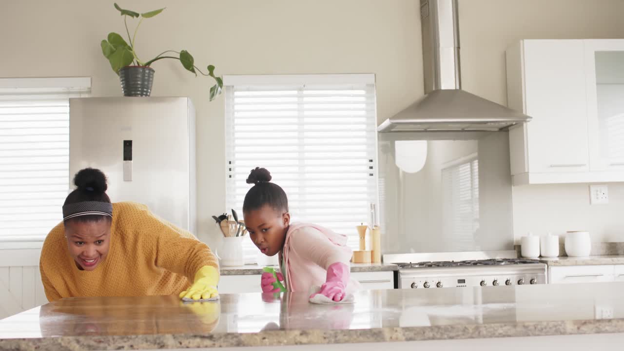 Happy african american mother and daughter cleaning countertop in kitchen, slow motion, copy space