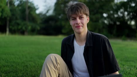 young man sitting on grass smiling at camera