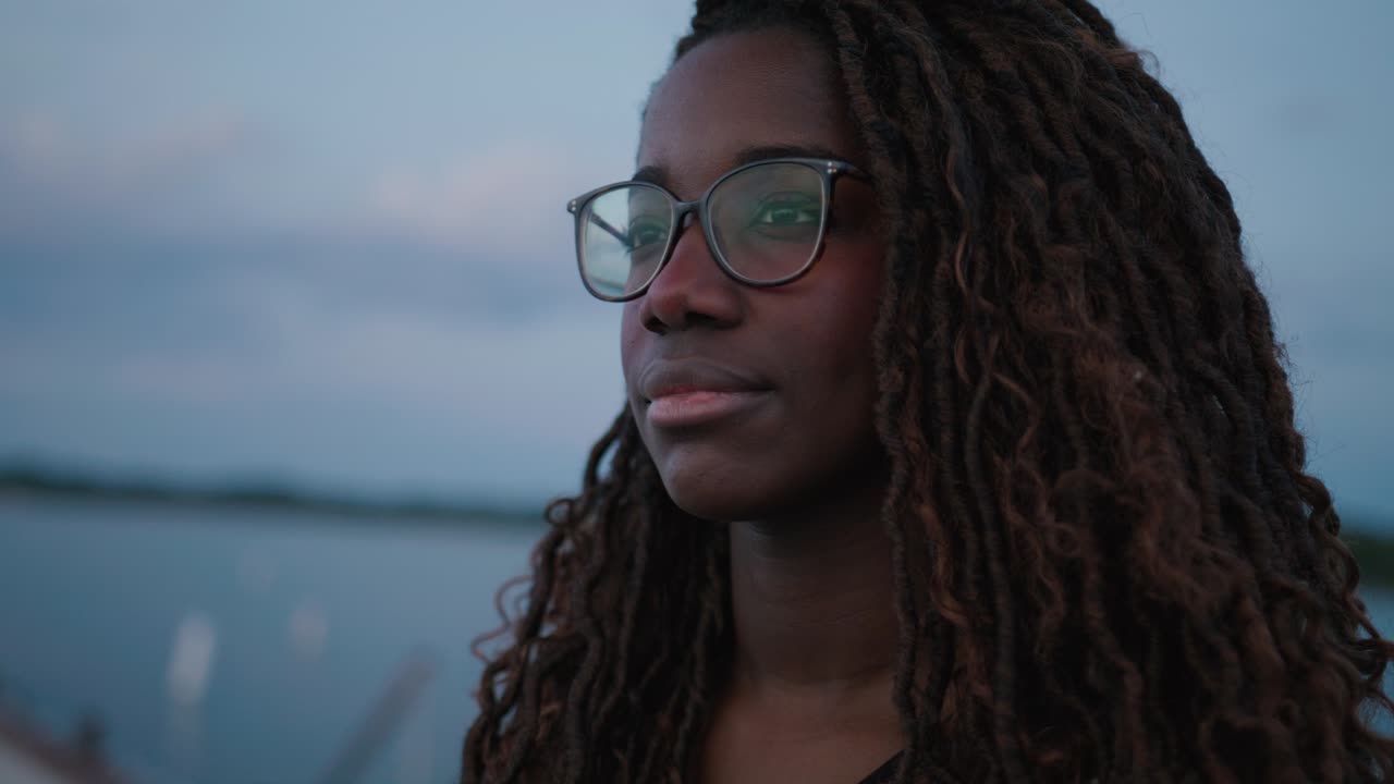 Young Adult black woman wearing glasses on a pier looking off into the distance with focused intent