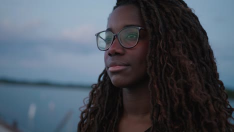 Mujer-Negra-Adulta-Joven-Con-Gafas-En-Un-Muelle-Mirando-A-Lo-Lejos-Con-Intención-Enfocada