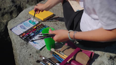 woman painting outdoors on a rock