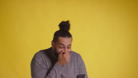 fotografía de un joven con un teléfono móvil celebrando la ganancia de dinero contra un fondo amarillo